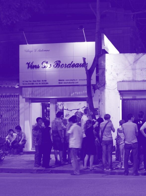 A group of people stand outside a store called "Vins Dr. Bordeaux." The image has a purple hue