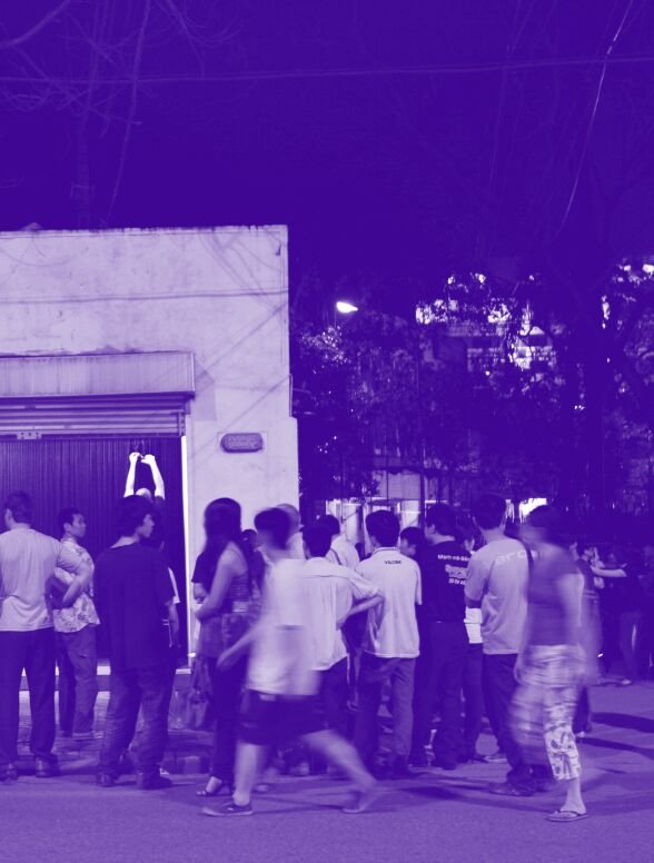 A group of pedestrians move around outside a garage. The image has a purple hue. 